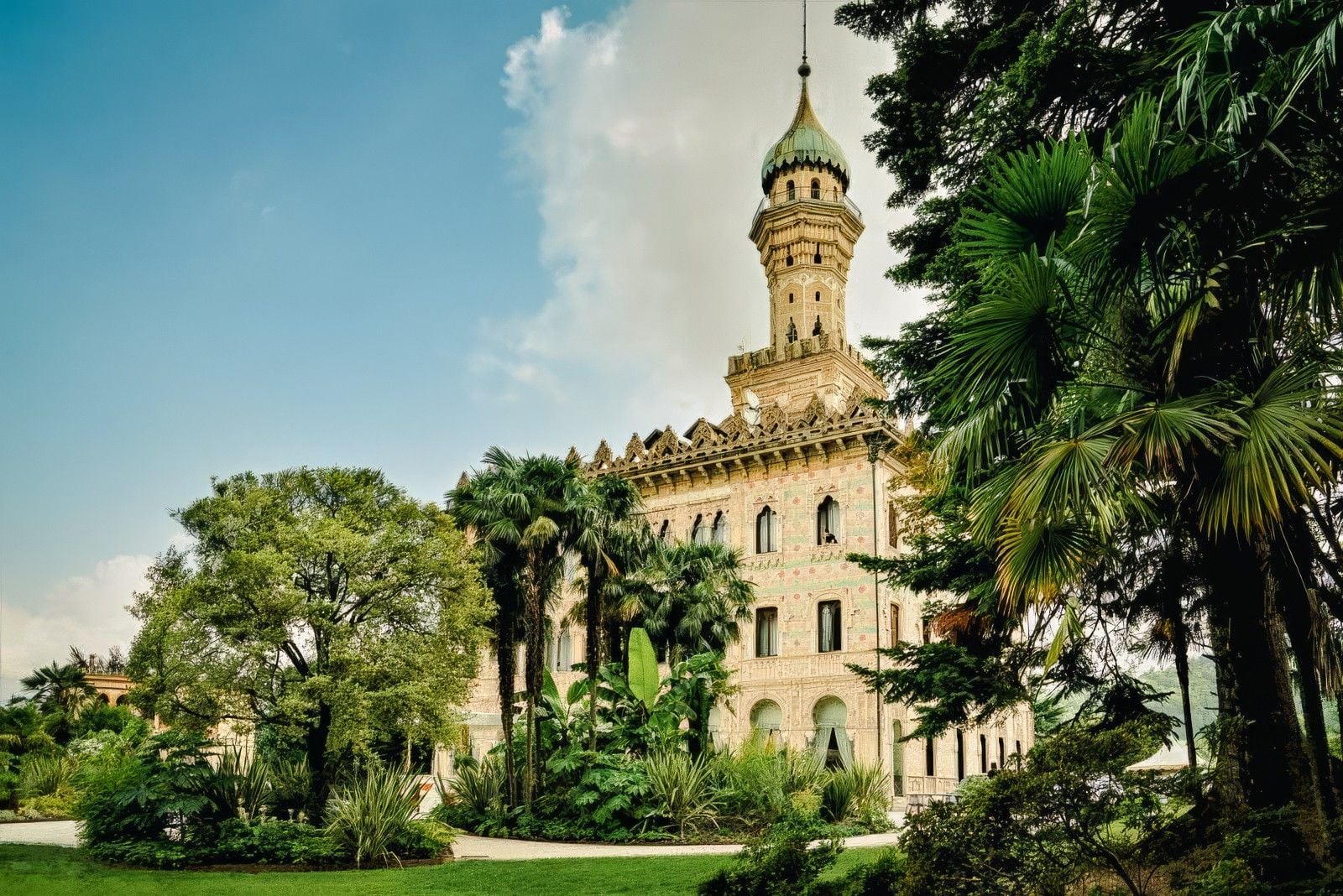 Historic building with a distinctive tower surrounded by lush greenery and palm trees under a blue sky.