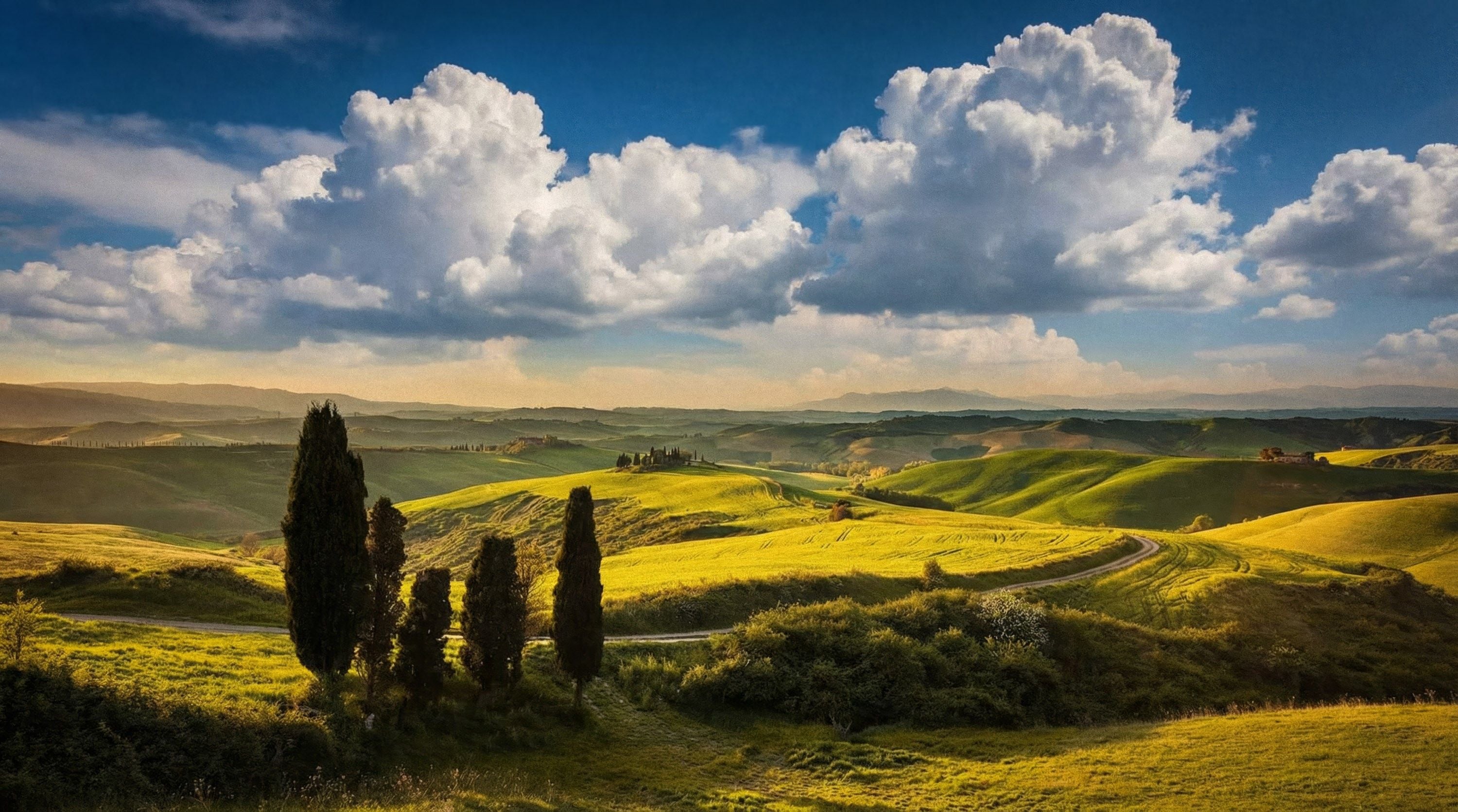 Rolling green hills under a vibrant sky filled with fluffy clouds at sunset, creating a serene landscape.