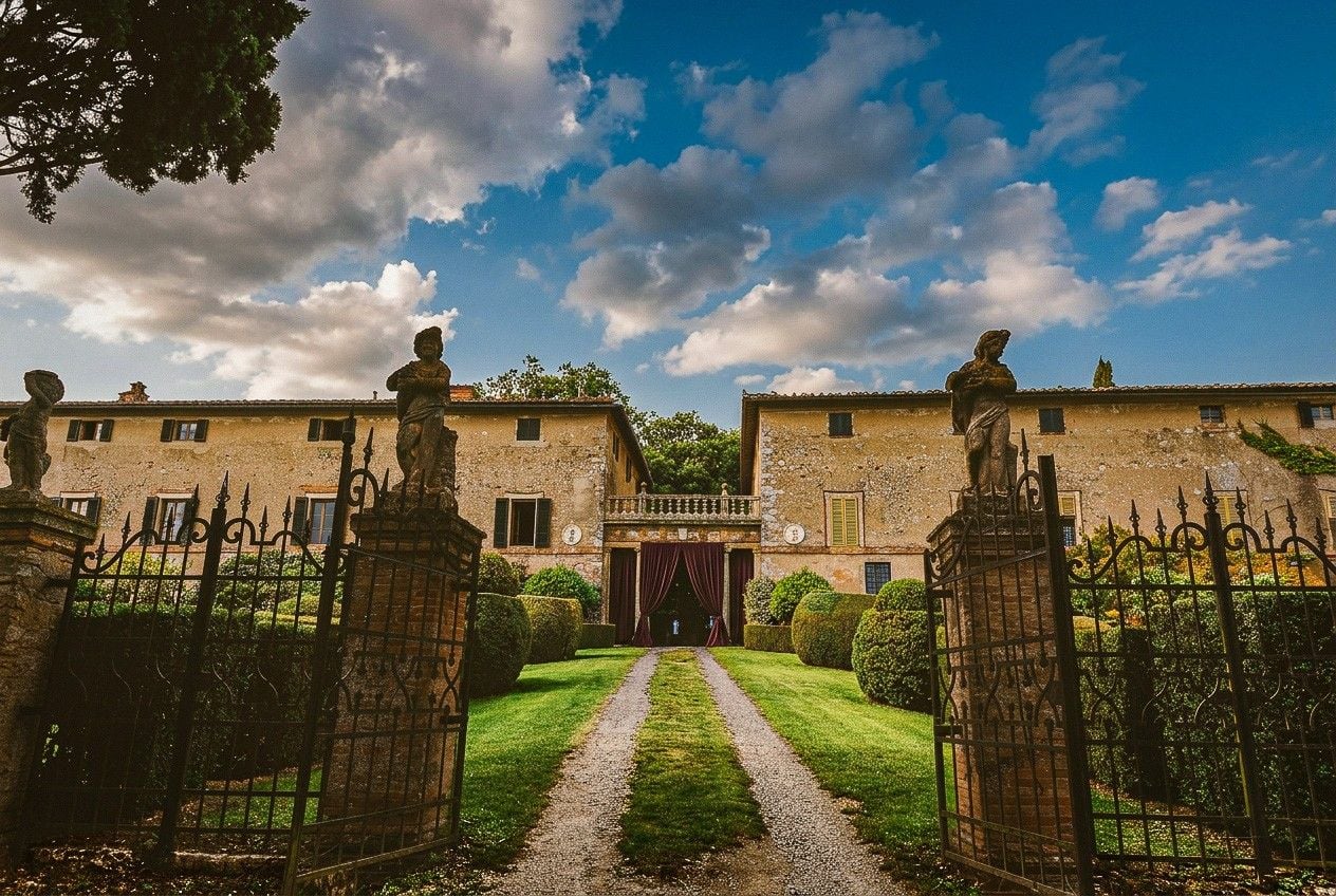 A romantic villa entrance with ornate gates, lush greenery, and a dramatic sky, creating an enchanting wedding setting.