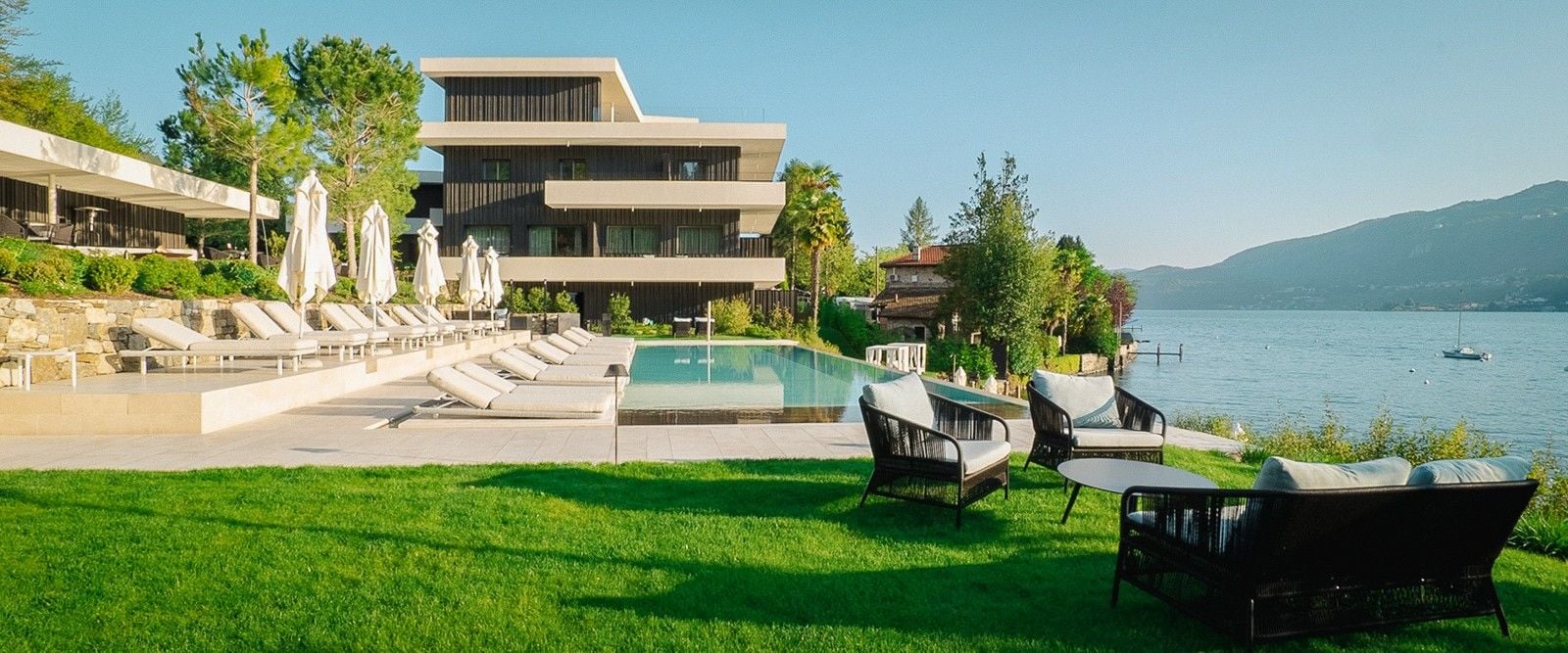 Luxurious lakeside villa with modern architecture, sun loungers by the pool, and scenic mountain views.