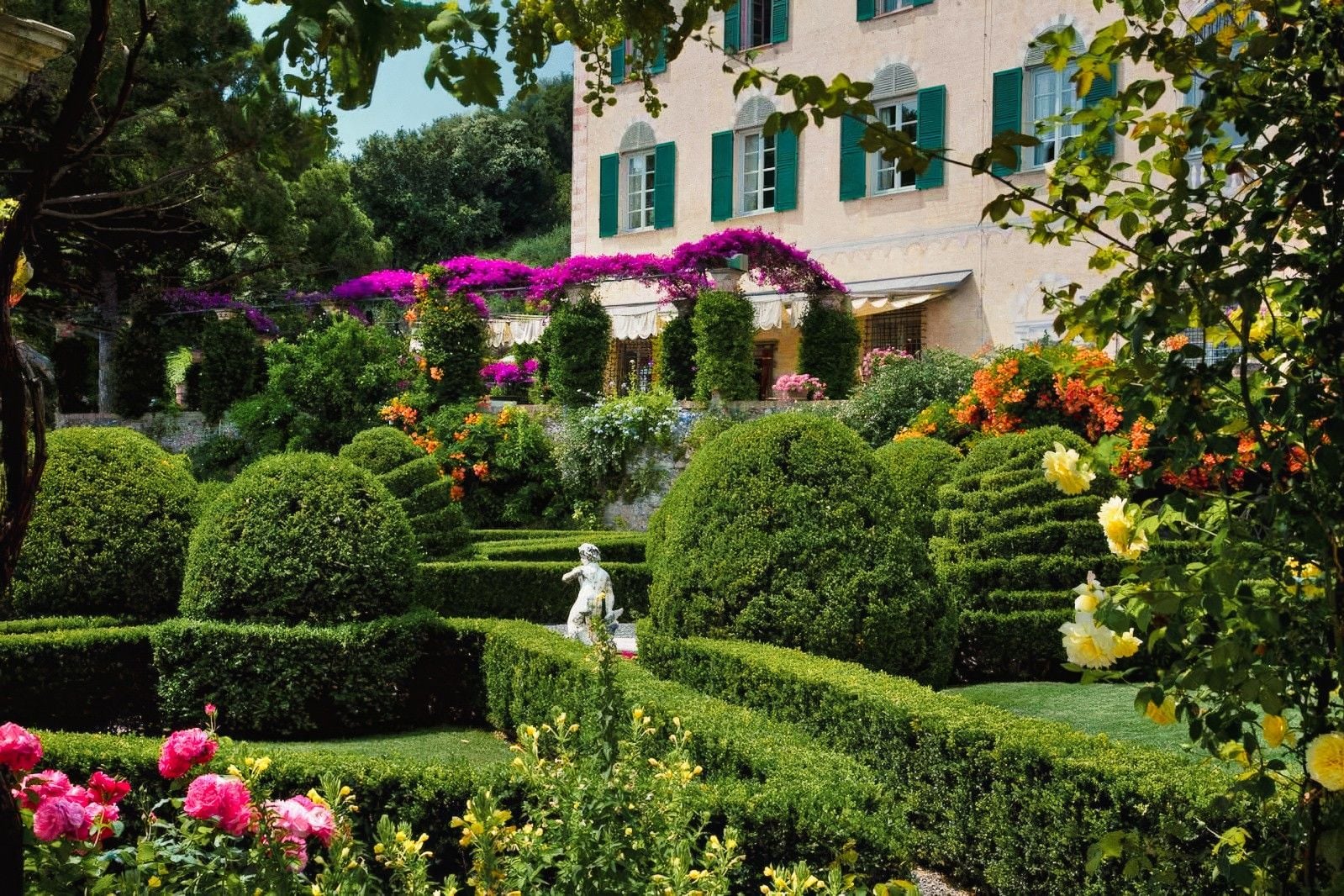 Lush garden featuring neatly trimmed hedges, vibrant flowers, and a charming statue amidst blooming greenery.