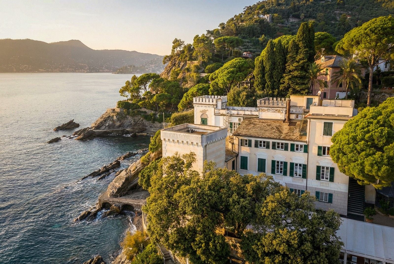 Scenic coastal view of a historic castle surrounded by lush greenery and rocky shores under a golden sunset.
