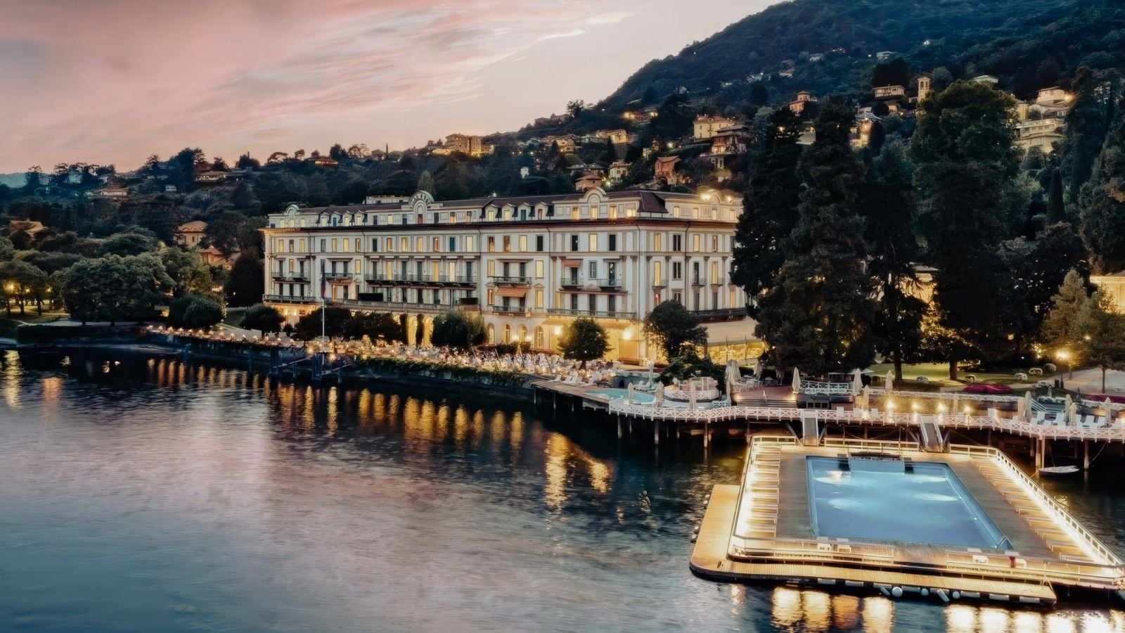 Luxurious hotel along a serene lake at twilight, featuring elegant architecture and moored boats.