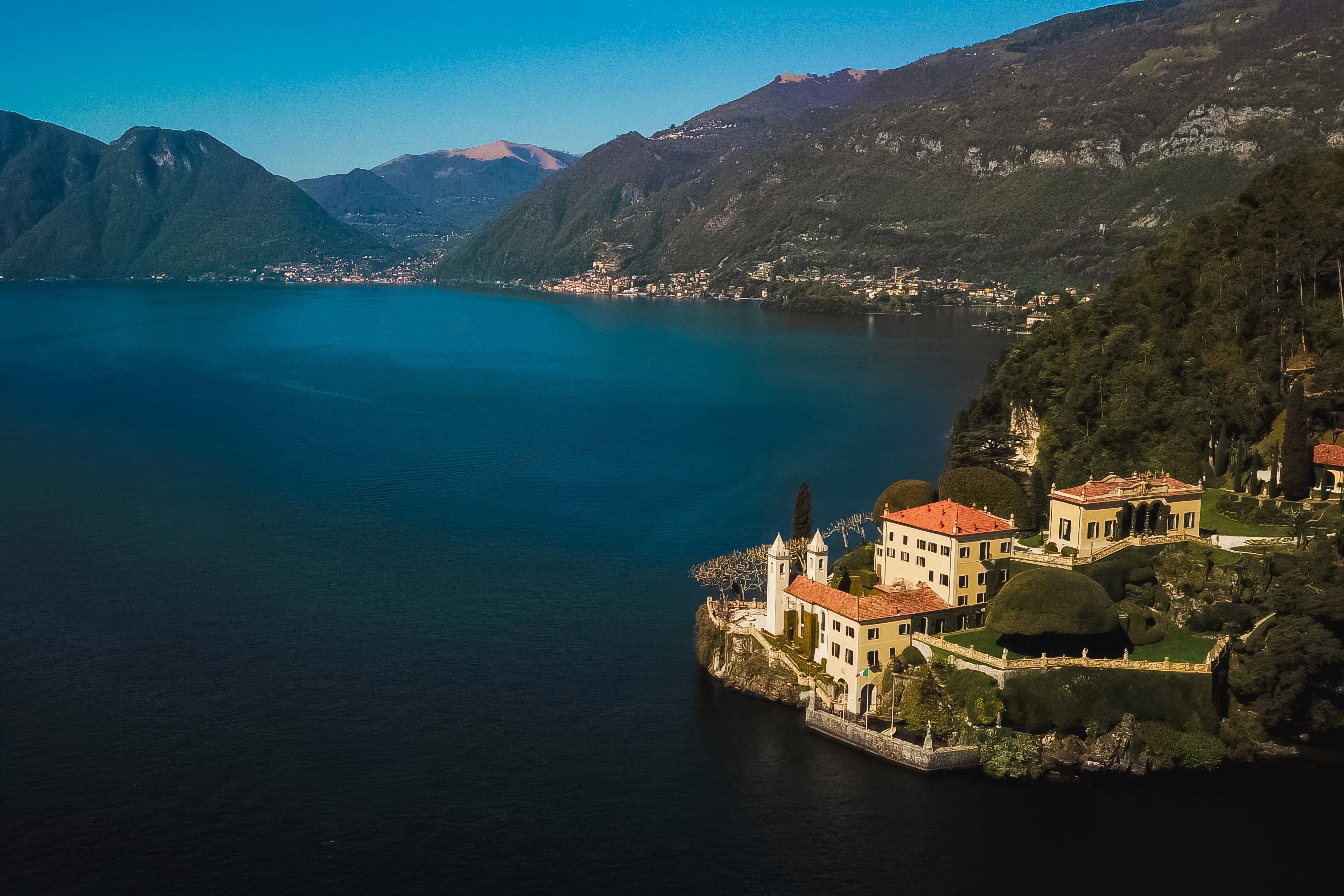 Lush green hills rise above a tranquil lake, showcasing a charming villa nestled along the water's edge.
