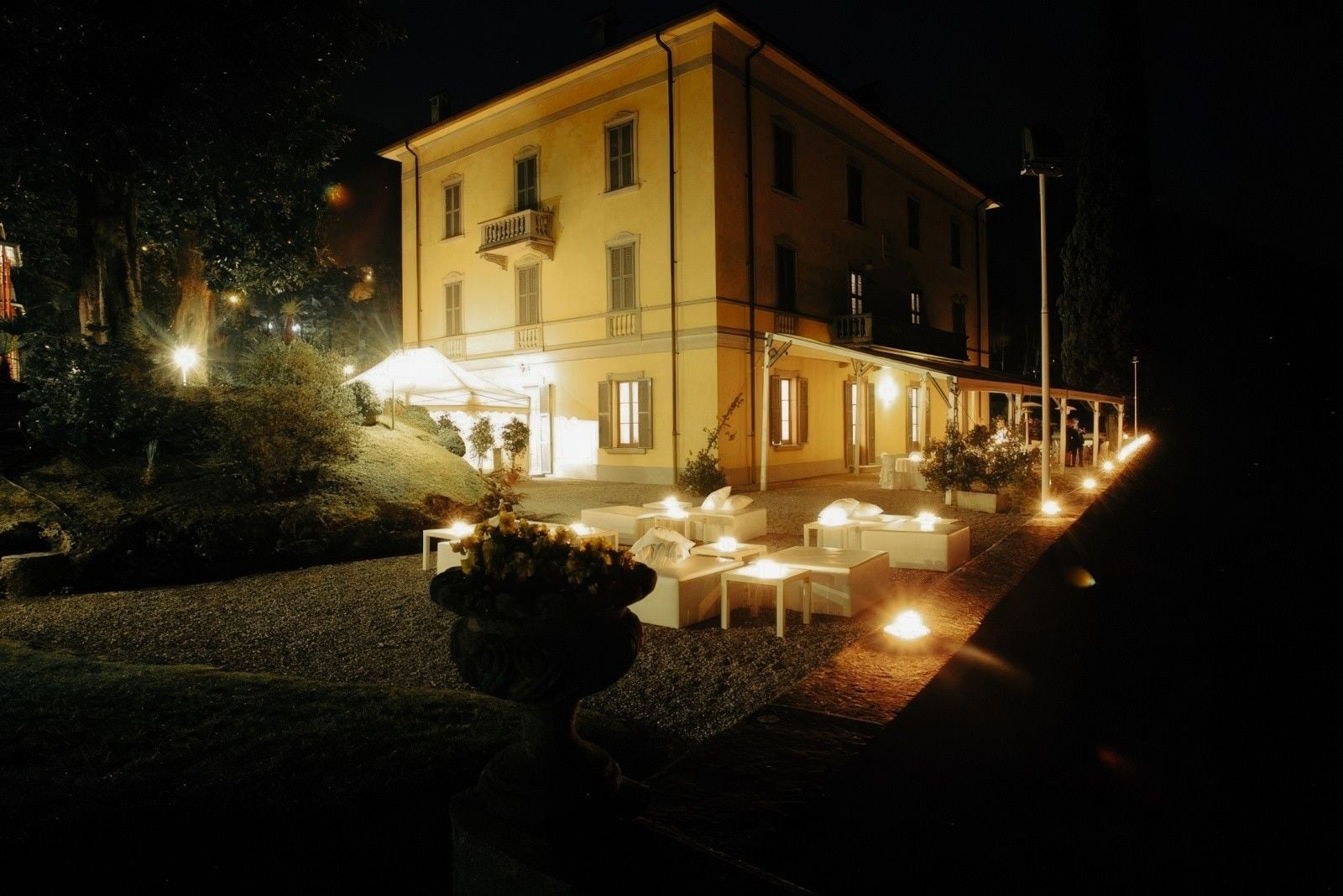 Elegant restaurant exterior at night, featuring illuminated seating area and lush garden ambiance.