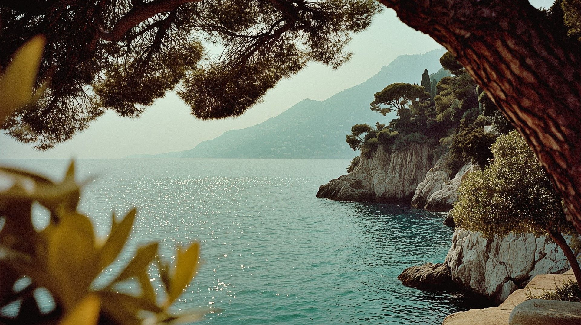Tranquil coastal scene featuring sunlit blue waters, rocky cliffs, and lush greenery under a clear sky.