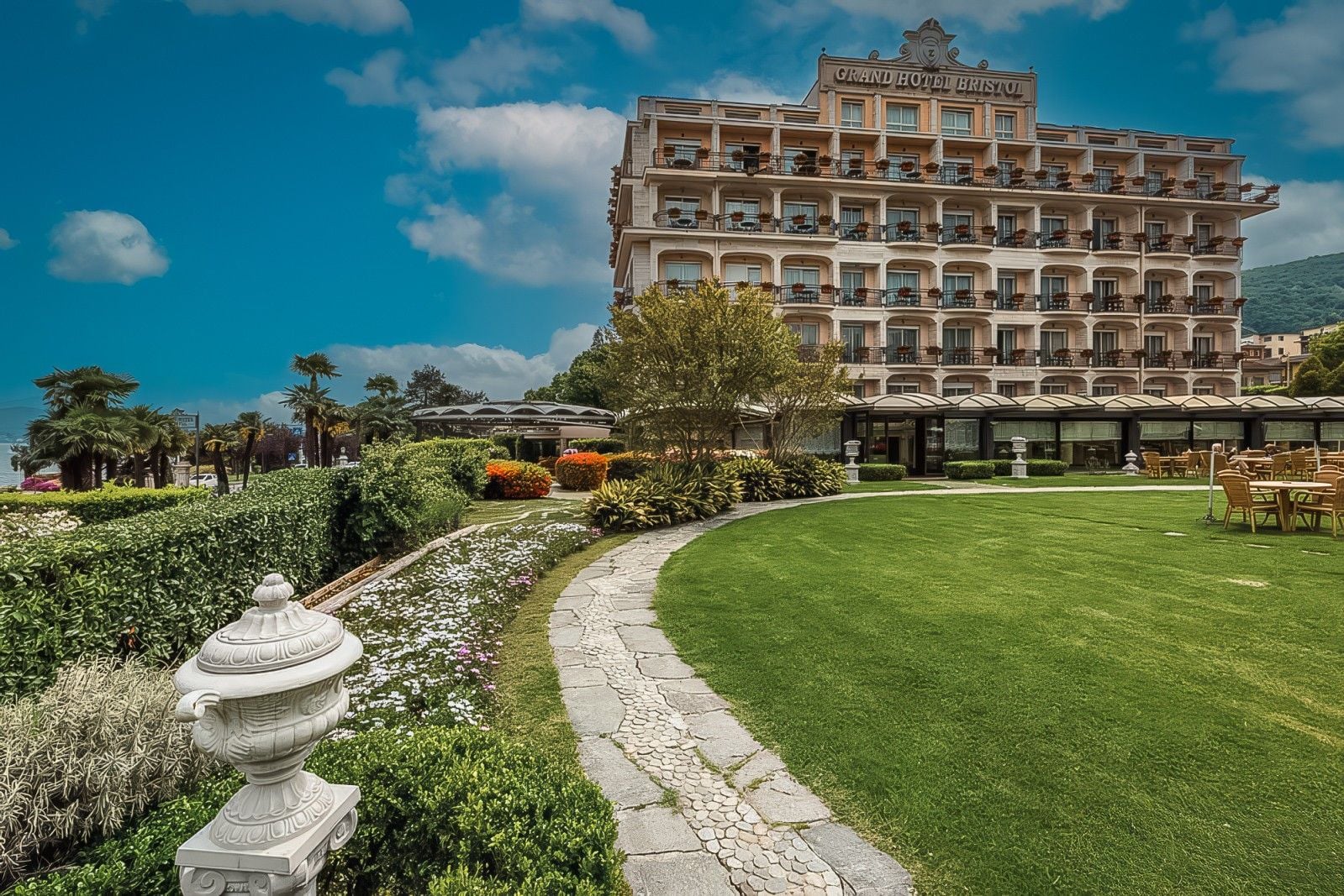 Luxurious hotel exterior surrounded by manicured gardens and vibrant flowers under a bright blue sky.