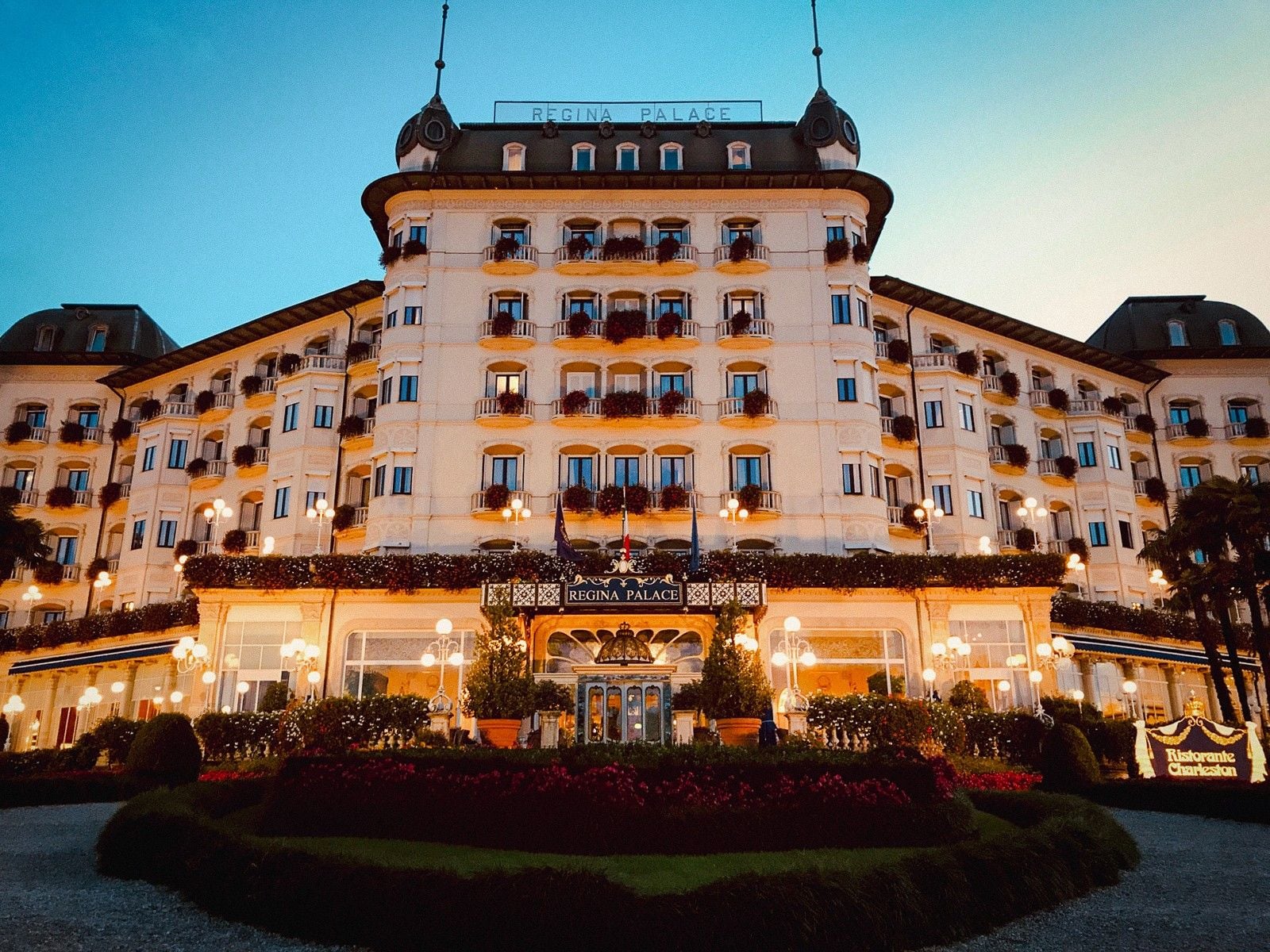 Elegant facade of the Regina Palace hotel illuminated at dusk, showcasing floral decorations and charming architecture.