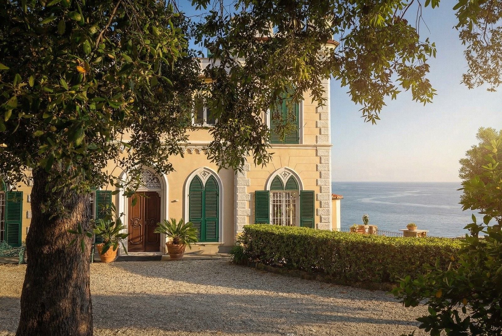 Charming coastal villa with green shutters, surrounded by lush greenery and a serene ocean view.