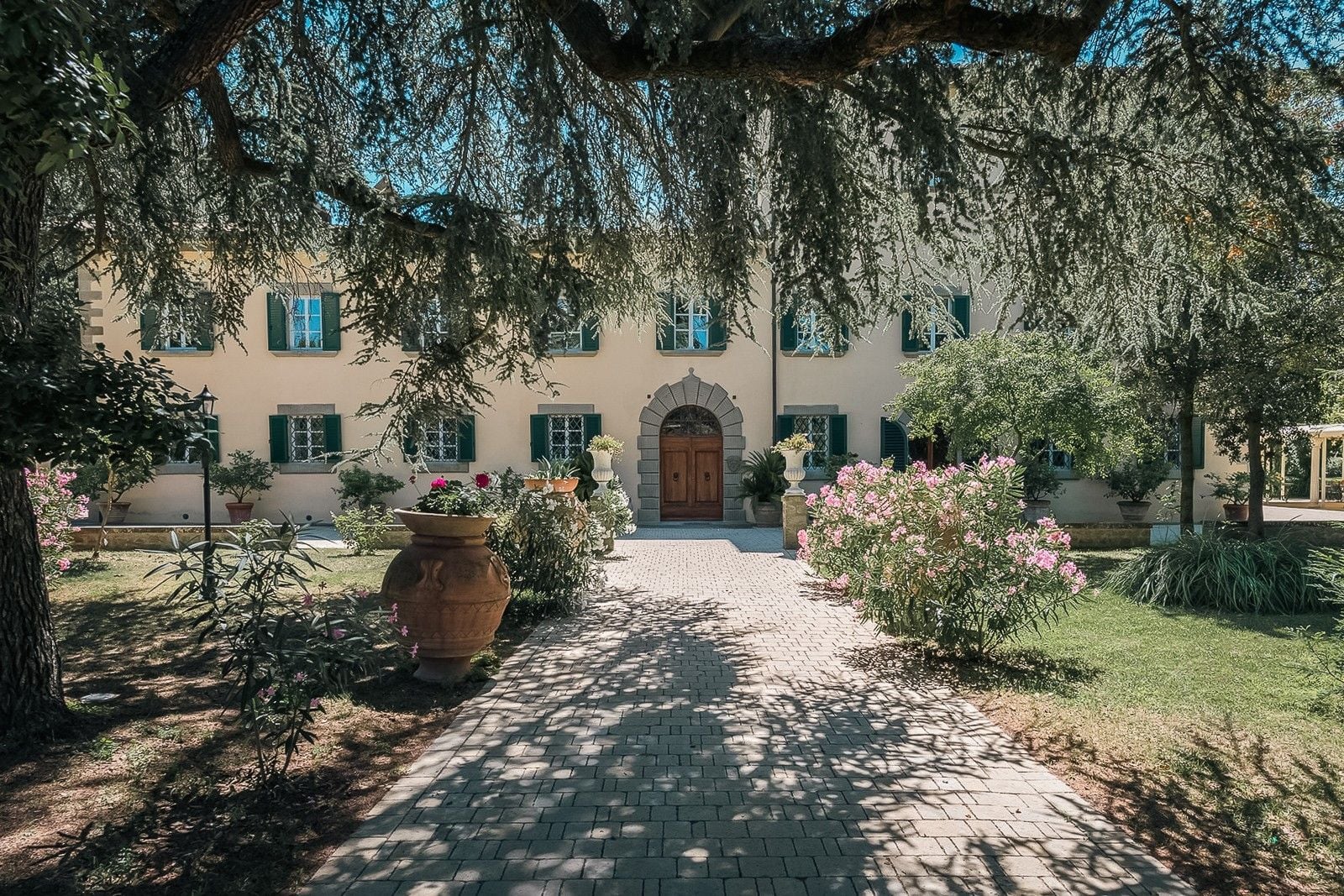 Charming villa entrance surrounded by lush greenery and colorful flowers, set against a clear blue sky.