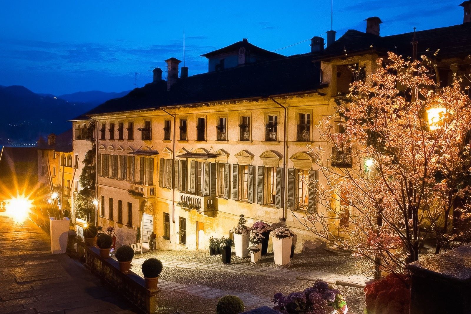 Charming historical building illuminated at dusk, surrounded by blossoming trees and cobblestone pathways.
