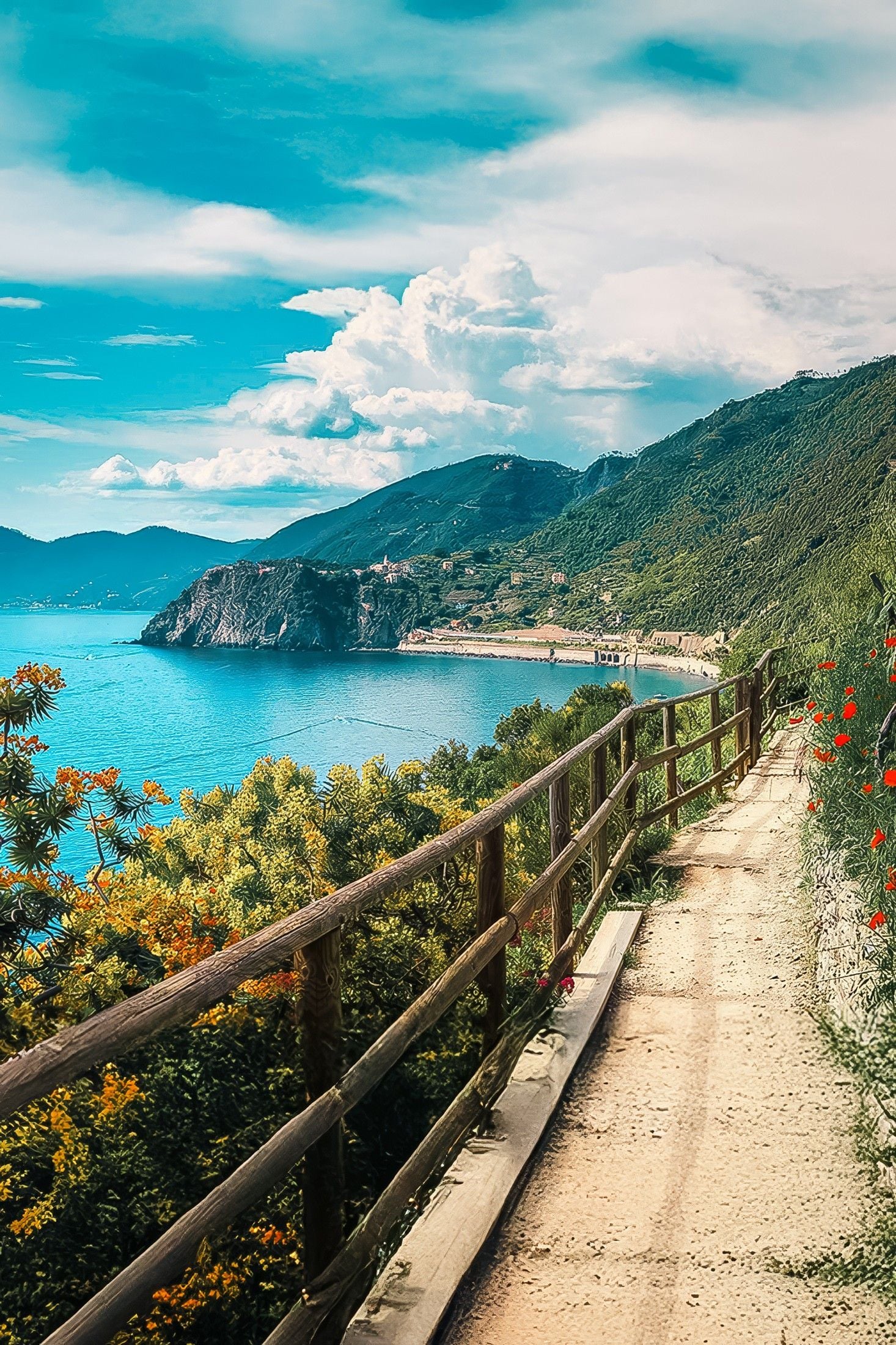 Scenic coastal pathway lined with vibrant flowers, overlooking tranquil blue waters and lush green hills.