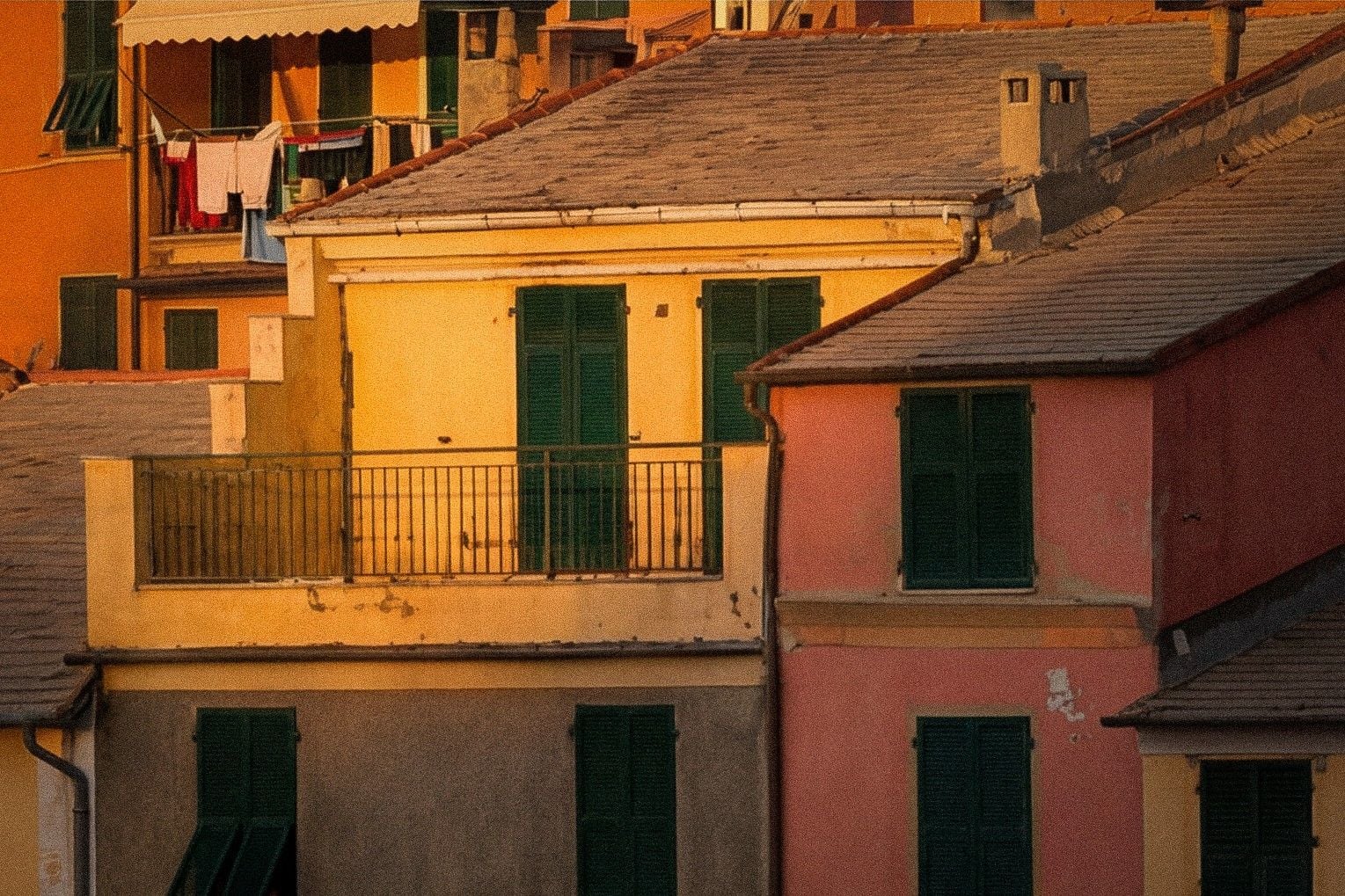 Sunlit balconies and colorful facades of hillside homes in a picturesque coastal village at sunset.