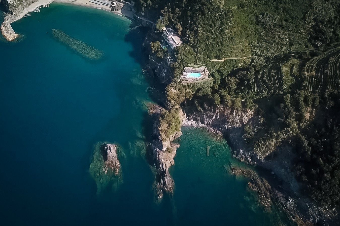 Aerial view of a coastal landscape featuring rocky shores, turquoise waters, and lush greenery along the coastline.