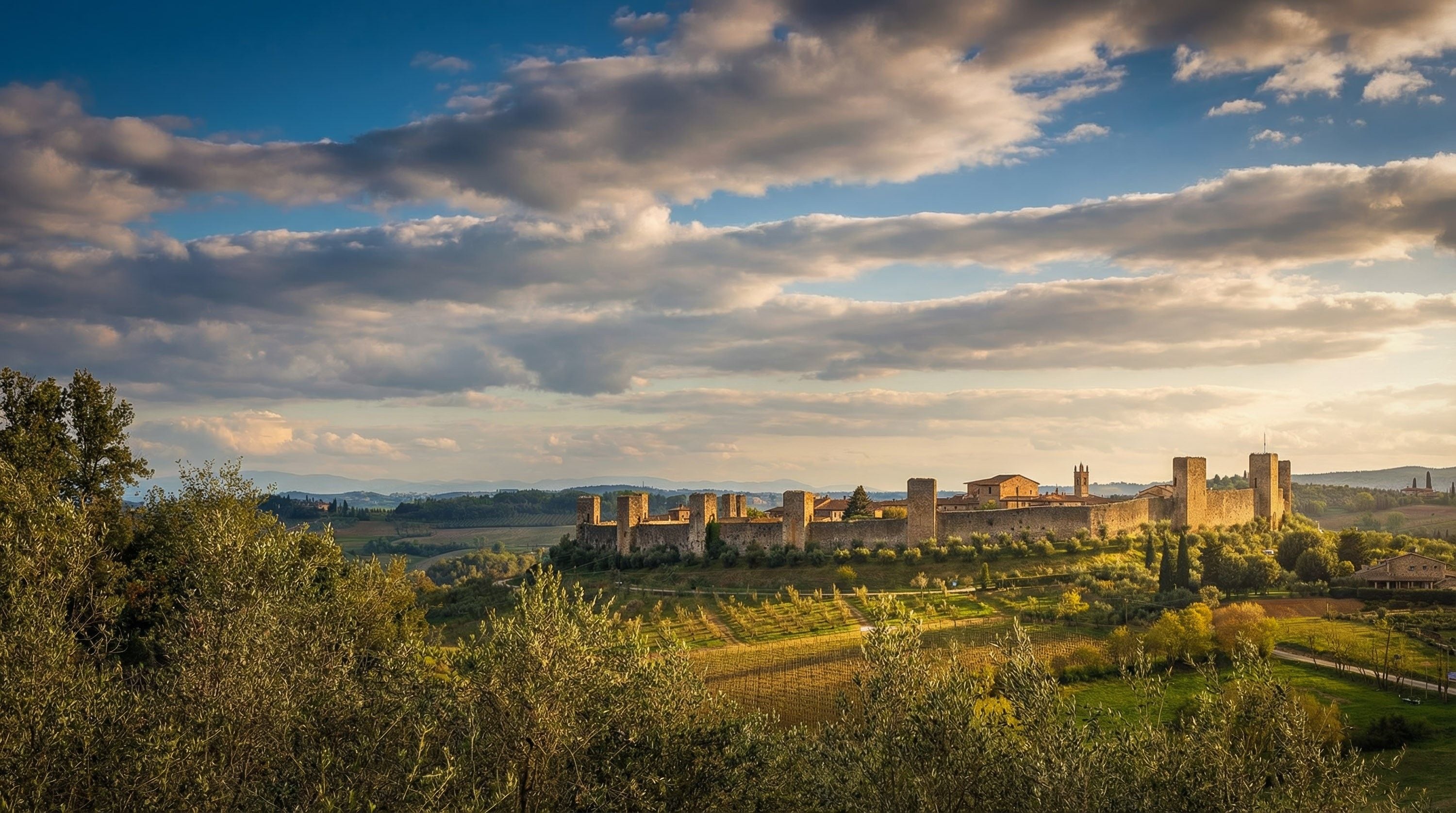 Sunset over a medieval castle surrounded by rolling hills and lush vineyards under a dramatic sky.